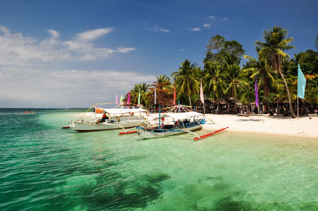 A group of colorful boats docked on a white sand beach in the Philippines. Book your flight to the Philippines today and experience the beauty of this tropical paradise.